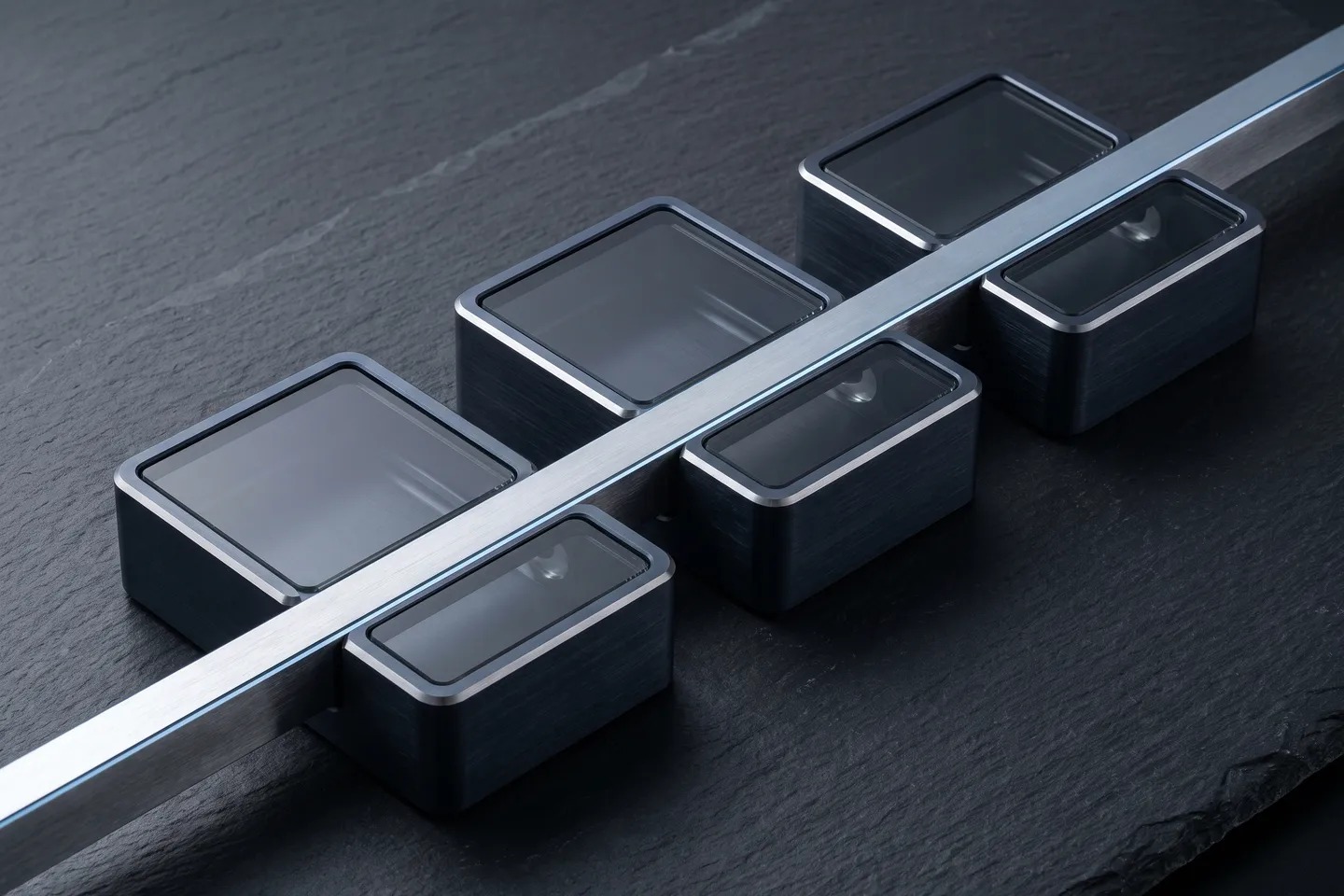 One steel rail runs through a row of sealed metal cases under dark glass